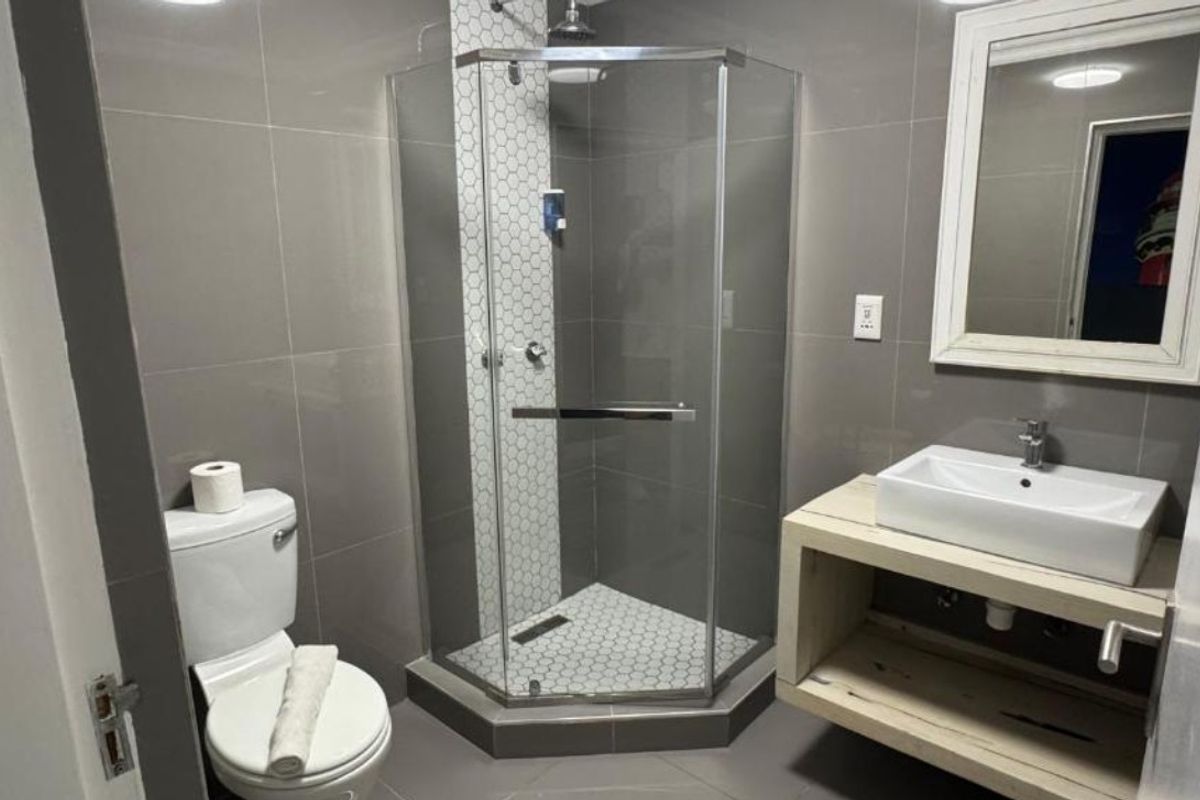 Modern bathroom featuring a corner glass shower enclosure, a vessel sink vanity, and neutral grey wall tiling.