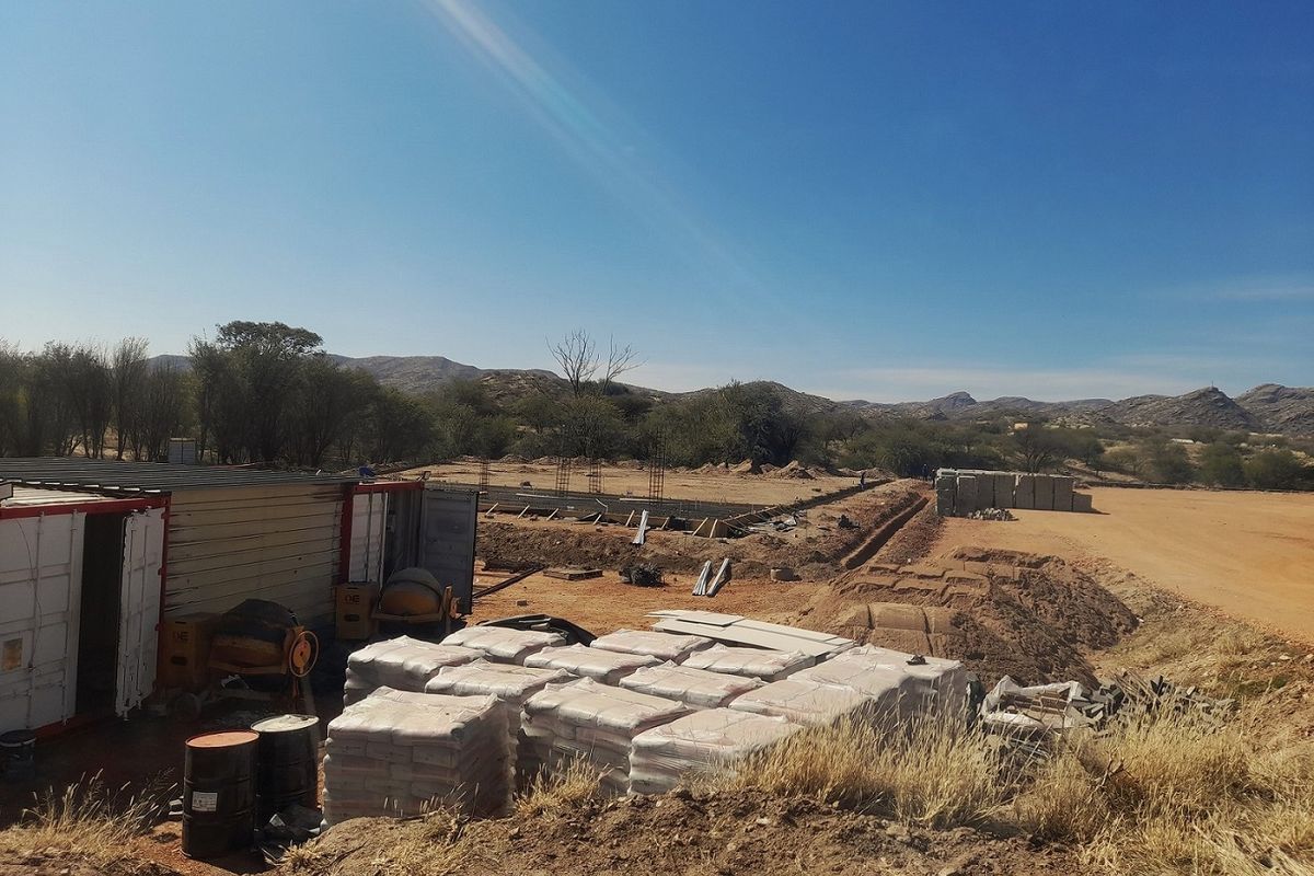 A vacant commercial land plot currently under development, featuring construction materials, site containers, and initial foundation work in a rural landscape setting.