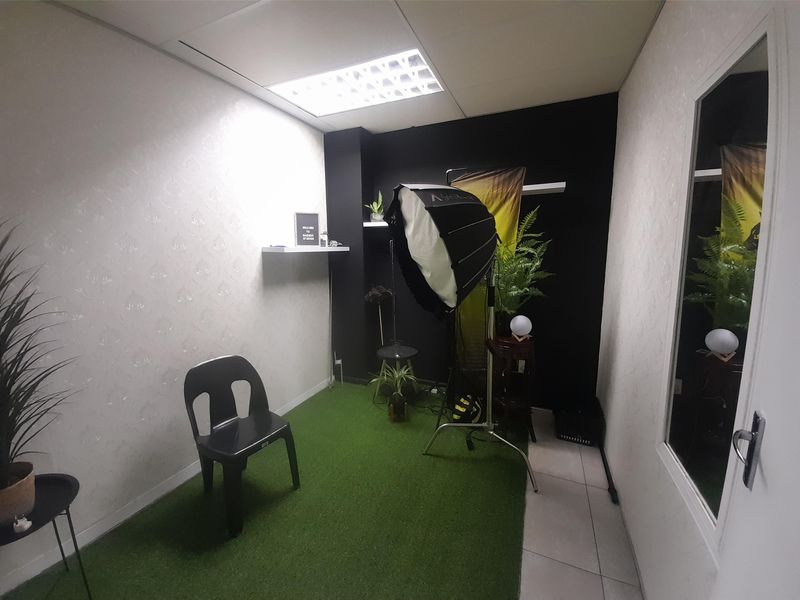 A compact office space featuring recessed ceiling lighting, floating wall shelves, and a glass-paneled door, currently utilized as a studio area.