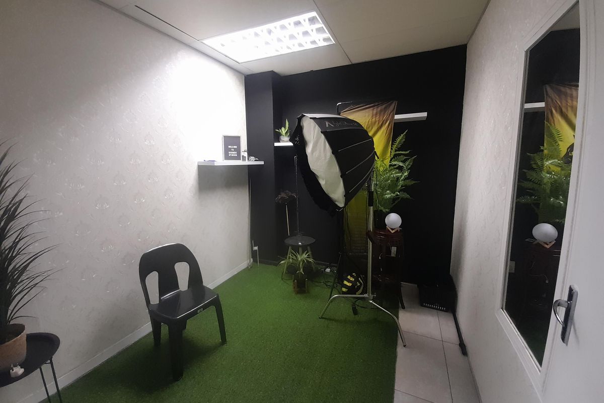 A compact office space featuring recessed ceiling lighting, floating wall shelves, and a glass-paneled door, currently utilized as a studio area.