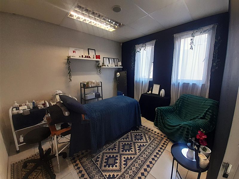 A functional office or treatment room featuring tiled flooring, a suspended ceiling with integrated lighting, and built-in wall shelving.