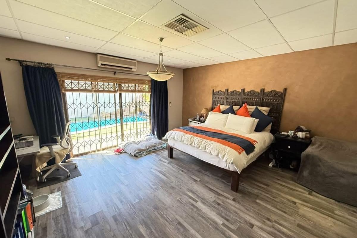 Spacious bedroom featuring laminate flooring, a suspended ceiling, air conditioning, and sliding glass doors with security gates leading to an outdoor area.