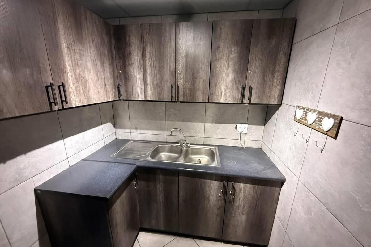 A compact, well-maintained kitchen area featuring modern wood-look cabinetry, a stainless steel double sink, and neutral tiled finishes.