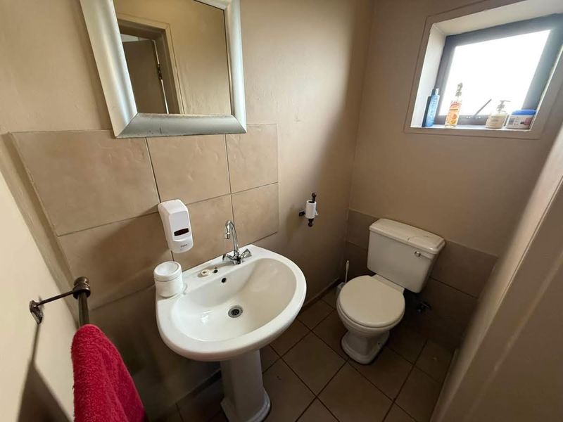 A functional industrial-style bathroom featuring a pedestal sink, toilet, tiled splashback, and tiled flooring with natural light from a side window.