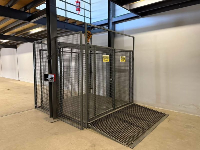 Industrial warehouse space featuring a functional steel mesh goods lift with integrated ramp and exposed structural steel beams.
