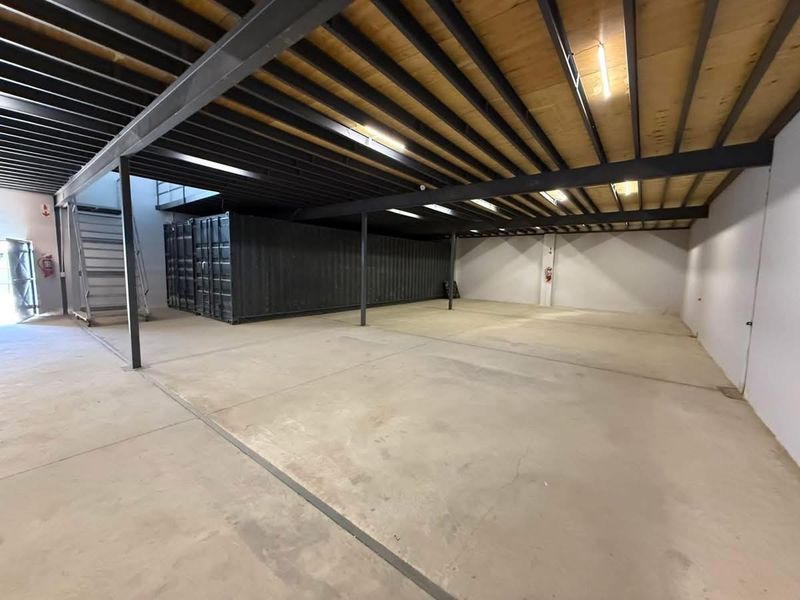 Spacious industrial utility area featuring exposed steel structural beams, a mezzanine level, concrete flooring, and an integrated shipping container storage unit.