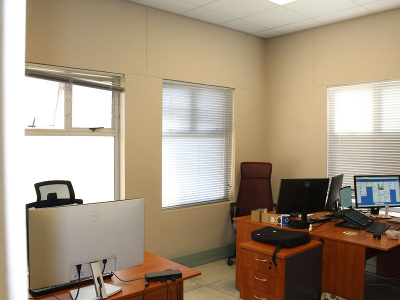 A functional office space featuring tiled flooring, suspended ceiling tiles, and multiple windows fitted with venetian blinds, providing natural light to the workspace.