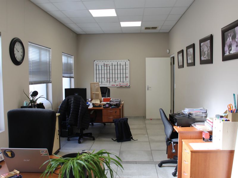 A functional office space featuring tiled flooring, suspended ceiling with recessed lighting, and large windows with venetian blinds.