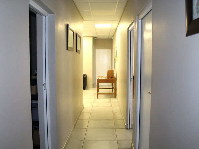 A functional office hallway featuring tiled flooring, a suspended ceiling with recessed lighting, and multiple internal access doors.