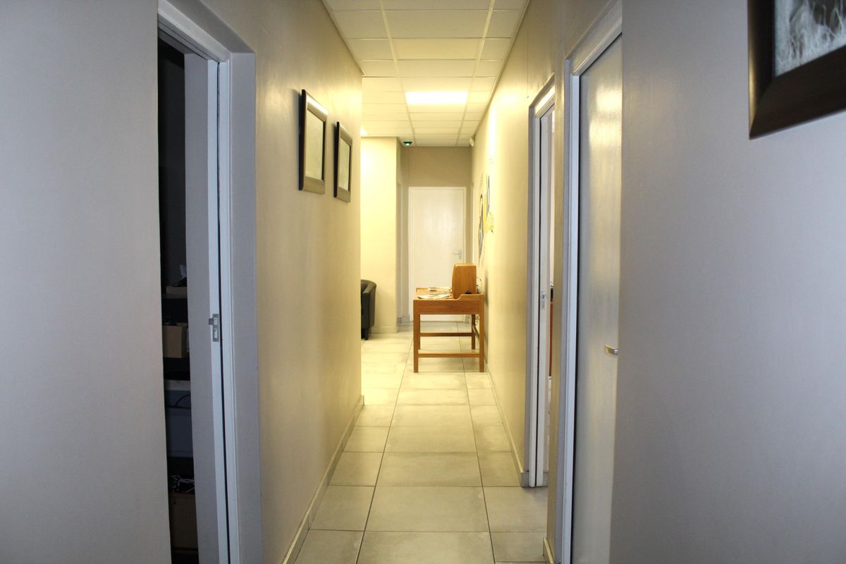 A functional office hallway featuring tiled flooring, a suspended ceiling with recessed lighting, and multiple internal access doors.