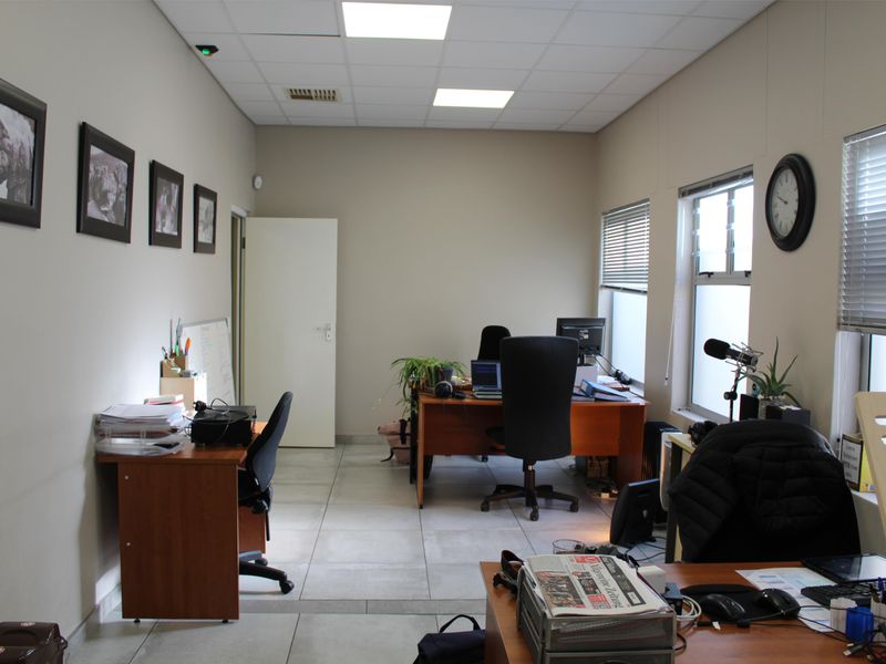 A functional office space featuring tiled flooring, a suspended ceiling with recessed lighting, and windows fitted with venetian blinds.