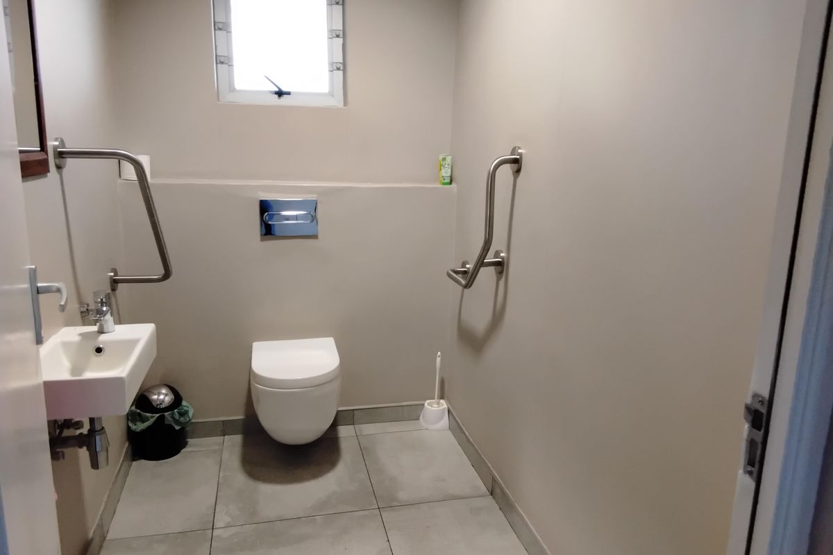 A clean, accessible bathroom featuring a wall-mounted toilet, wall-mounted basin, and stainless steel grab rails with neutral tiled flooring.