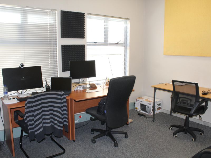 A functional office space featuring carpeted flooring, venetian blinds, and acoustic wall panels, suitable for a professional work environment.