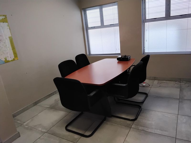 A functional office meeting room featuring tiled flooring and large windows with fitted venetian blinds, providing natural light for a professional workspace.
