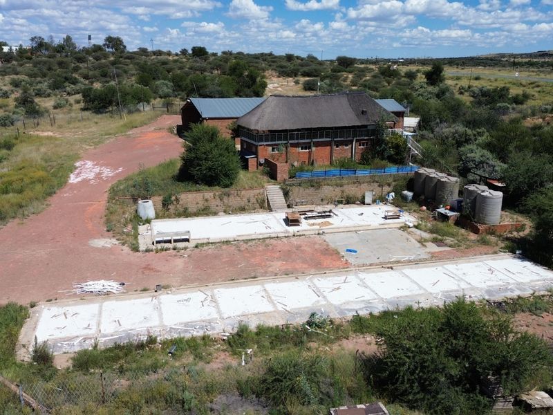 Aerial view of an industrial property featuring a thatched-roof building, multiple concrete slabs, and water storage tanks on a large plot of land.