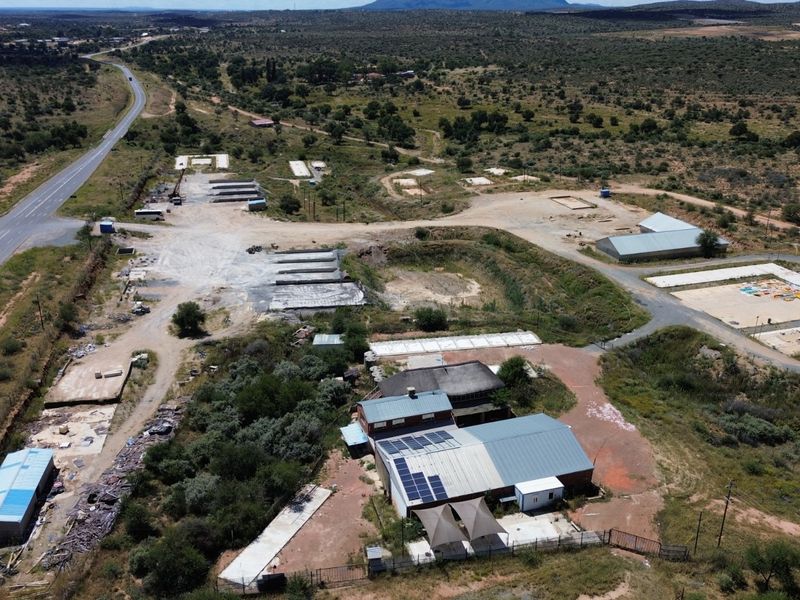 Aerial view of an industrial property featuring multiple structures, solar panel installations, and extensive surrounding land with direct road access.