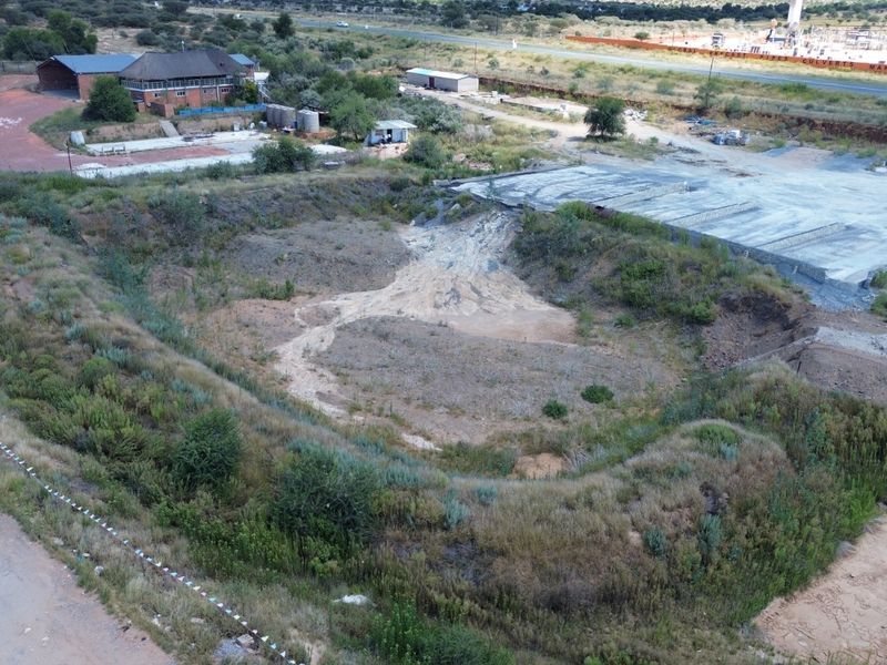Aerial view of an industrial site featuring a large concrete slab, surrounding undeveloped land, and perimeter fencing with access road frontage.