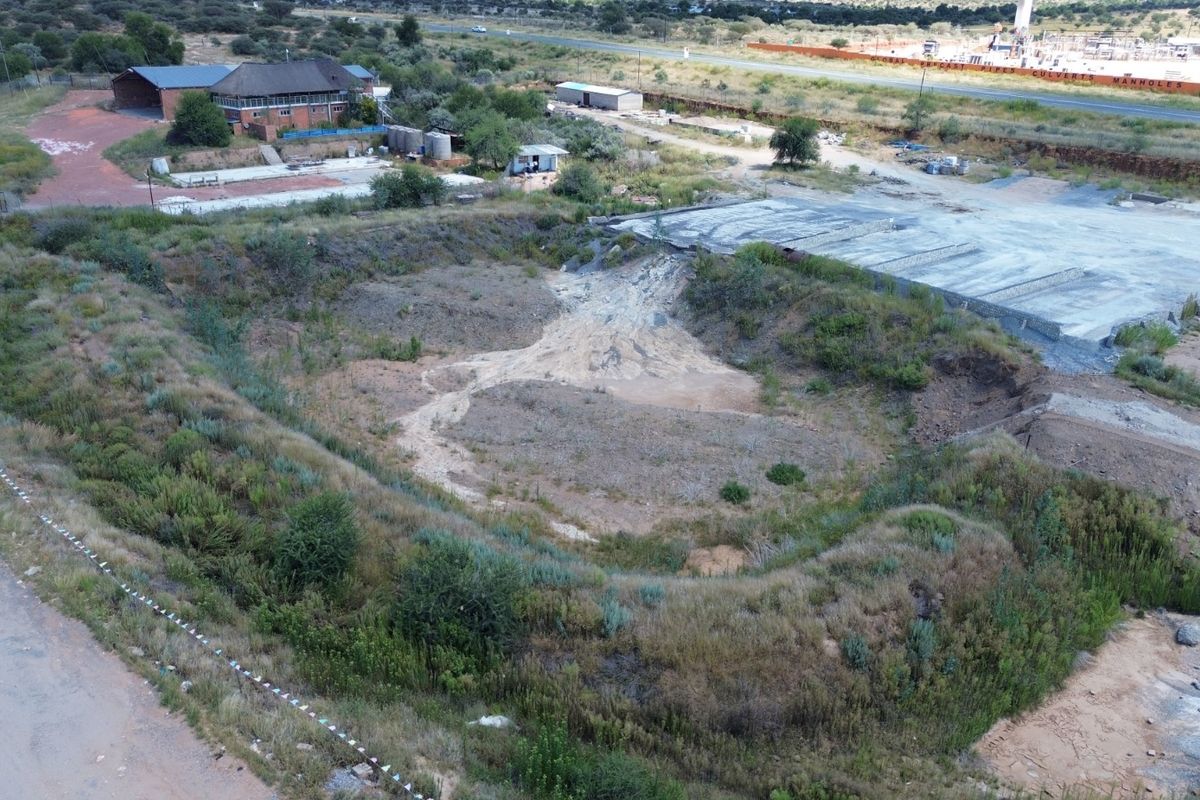 Aerial view of an industrial site featuring a large concrete slab, surrounding undeveloped land, and perimeter fencing with access road frontage.