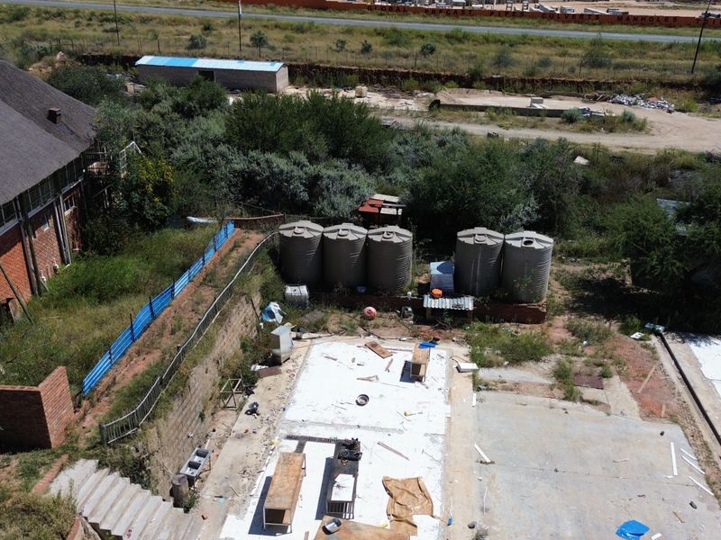 Aerial view of an industrial site featuring multiple water storage tanks, a concrete slab foundation, and surrounding overgrown land with perimeter fencing.