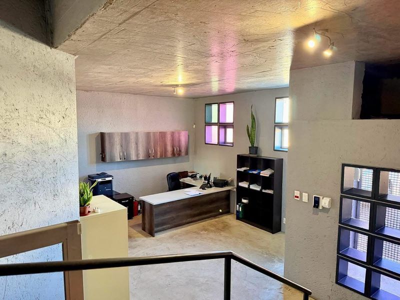 Industrial-style office space featuring textured concrete walls, exposed ceiling, built-in wall cabinetry, and a functional workspace layout.