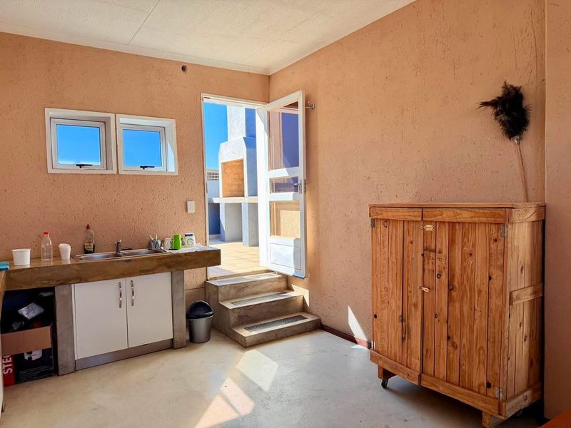 A functional scullery area featuring a concrete countertop with an integrated sink, built-in cabinetry, and direct access to an outdoor patio area.