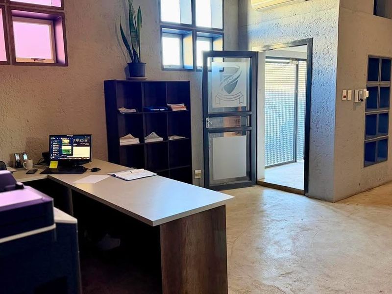 Industrial-style office space featuring textured concrete walls, polished concrete flooring, built-in shelving, and large windows providing natural light.