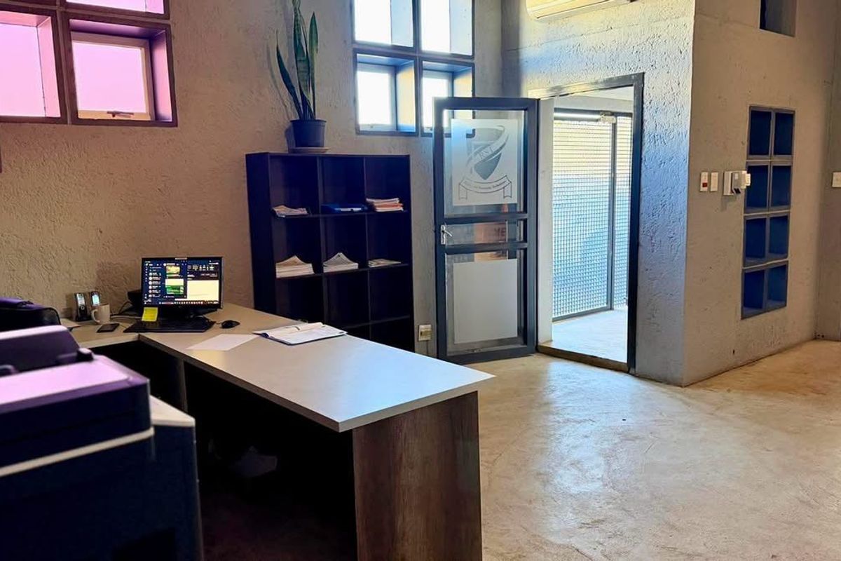 Industrial-style office space featuring textured concrete walls, polished concrete flooring, built-in shelving, and large windows providing natural light.