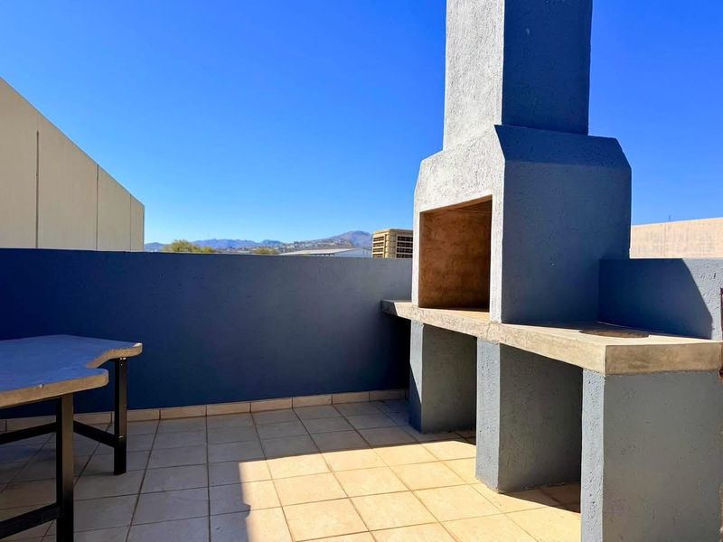 An outdoor balcony area featuring a built-in braai, tiled flooring, and a concrete counter, offering an open space for entertainment.