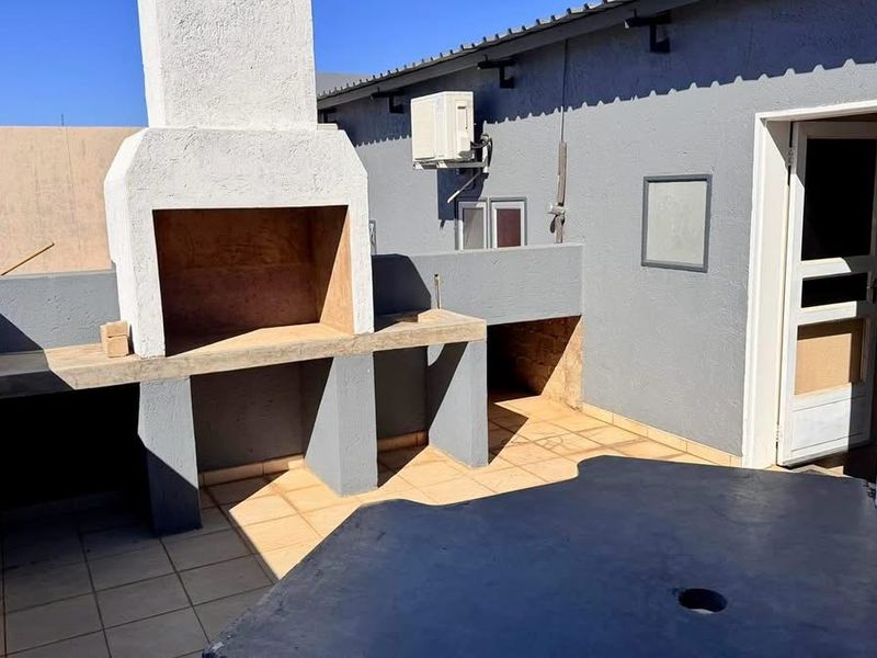 Outdoor patio area featuring a built-in braai, tiled flooring, and an exterior air conditioning unit, providing a functional space for outdoor entertainment.