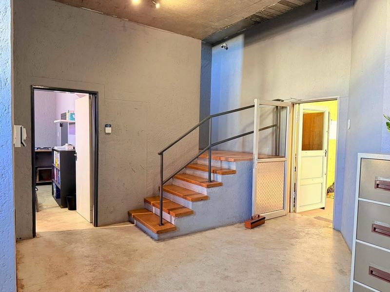 An industrial-style office space featuring exposed concrete ceilings, concrete flooring, and a central staircase with a metal handrail leading to an upper level.