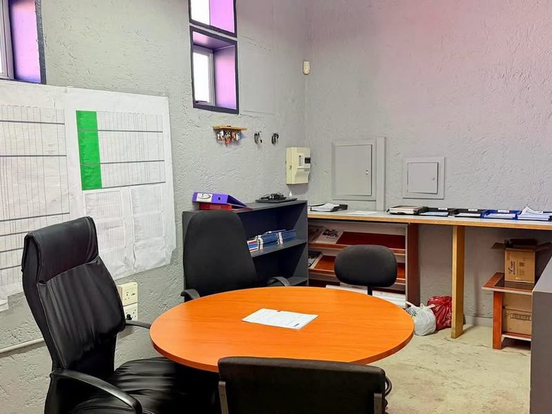 Functional industrial office space featuring a built-in desk, high-level windows, and exposed electrical infrastructure, suitable for administrative or operational use.
