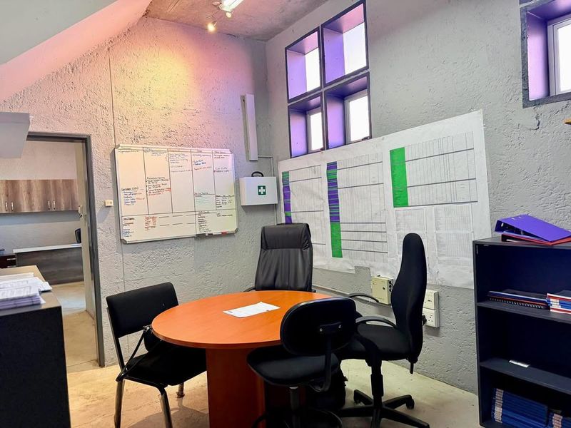 Functional industrial-style office space featuring textured concrete walls, exposed ceiling, and multi-pane windows, suitable for a professional workspace.