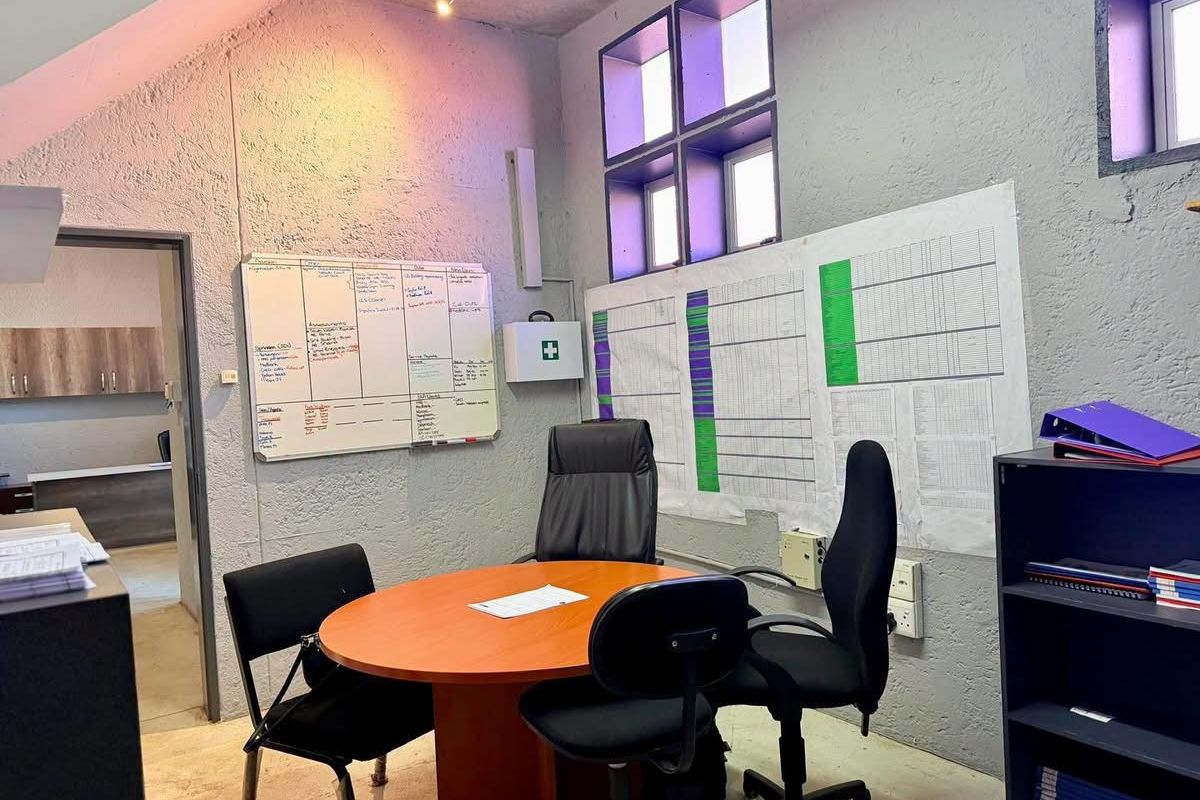 Functional industrial-style office space featuring textured concrete walls, exposed ceiling, and multi-pane windows, suitable for a professional workspace.
