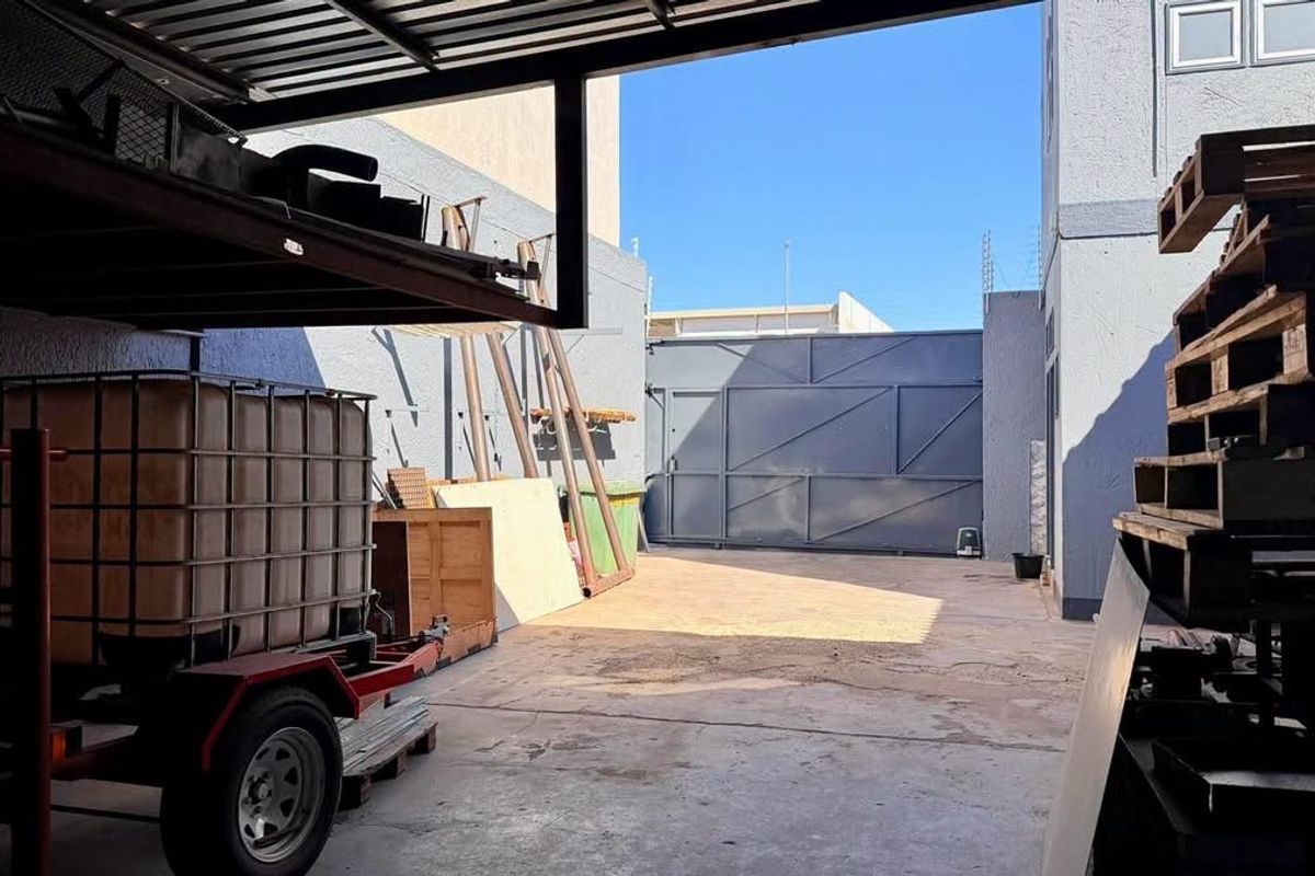 A secure industrial rear yard featuring a concrete hardstand, perimeter walls, and a large metal sliding gate for vehicle access.