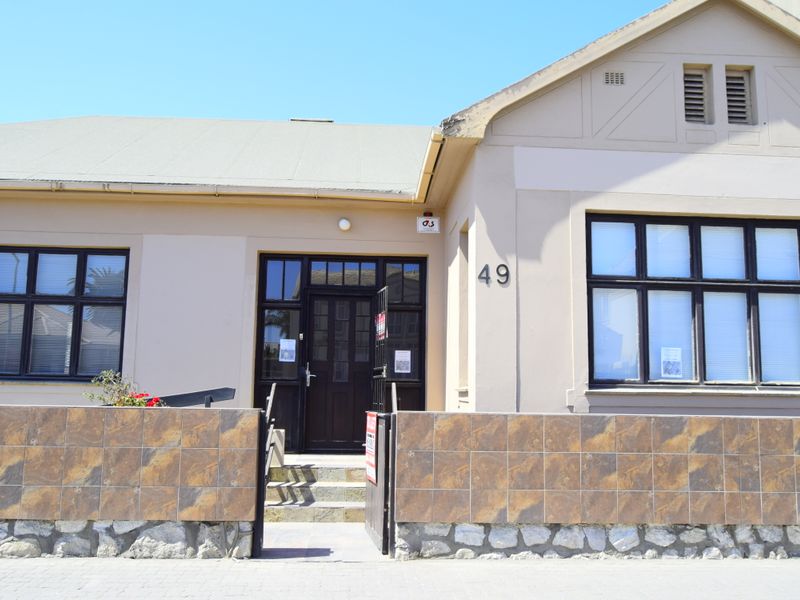 Front elevation of a commercial property featuring a tiled boundary wall, stone base, and traditional timber entrance door with multi-pane windows.