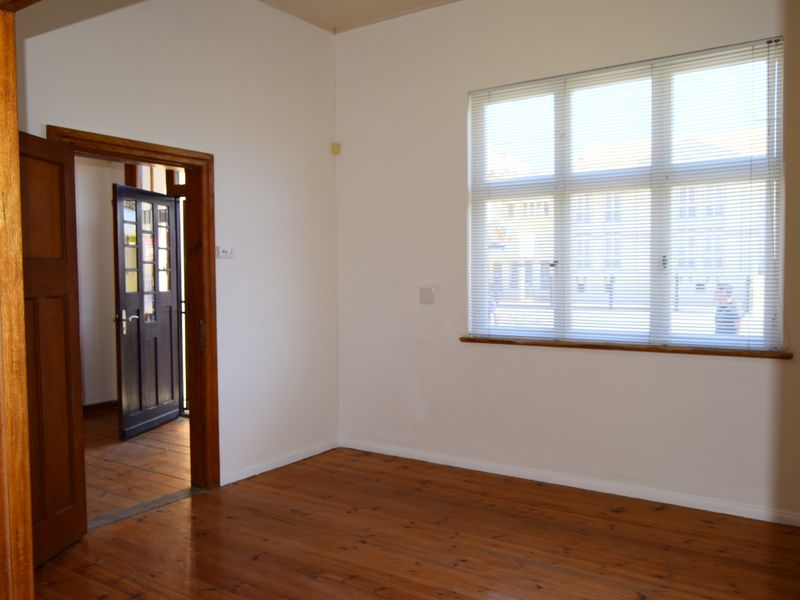 A bright, empty office space featuring polished timber flooring, wooden door frames, and a large multi-pane window with fitted venetian blinds.