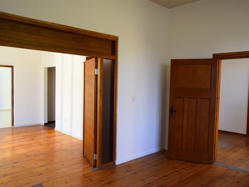 An empty interior hallway featuring polished timber flooring and traditional solid wood door frames connecting multiple rooms.