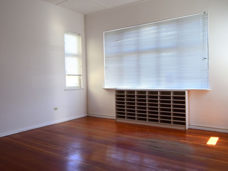 A bright, empty office space featuring polished timber flooring, built-in pigeonhole shelving, and large windows with fitted venetian blinds.