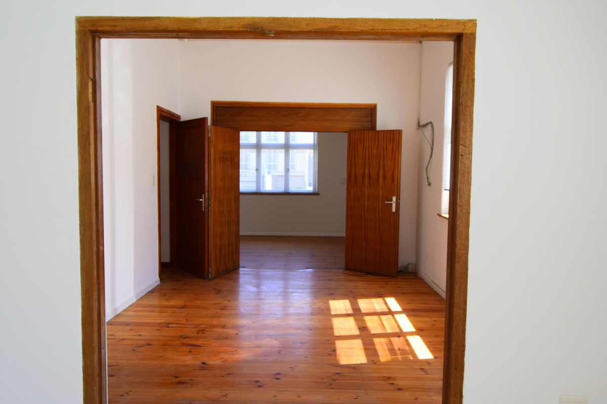 An empty, sunlit room featuring polished timber flooring and classic wooden door frames, offering a versatile space for commercial or office use.