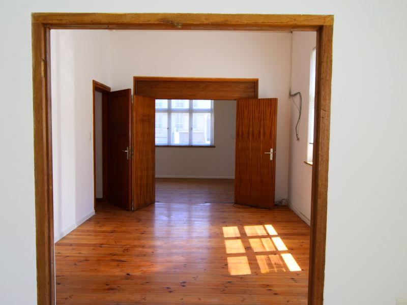 An empty, sunlit room featuring polished timber flooring and classic wooden door frames, offering a versatile space for commercial or office use.