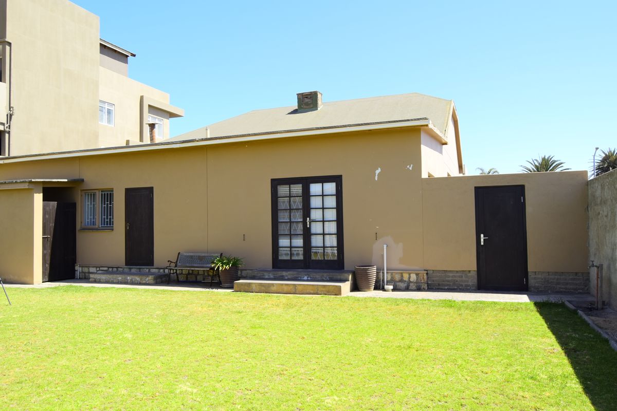 Rear exterior view of the property featuring a lawn, stone-based wall cladding, french doors, and a chimney.
