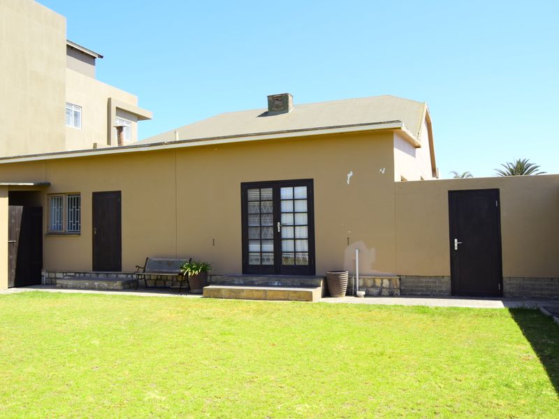 Rear exterior view of the property featuring a lawn, stone-based wall cladding, french doors, and a chimney.