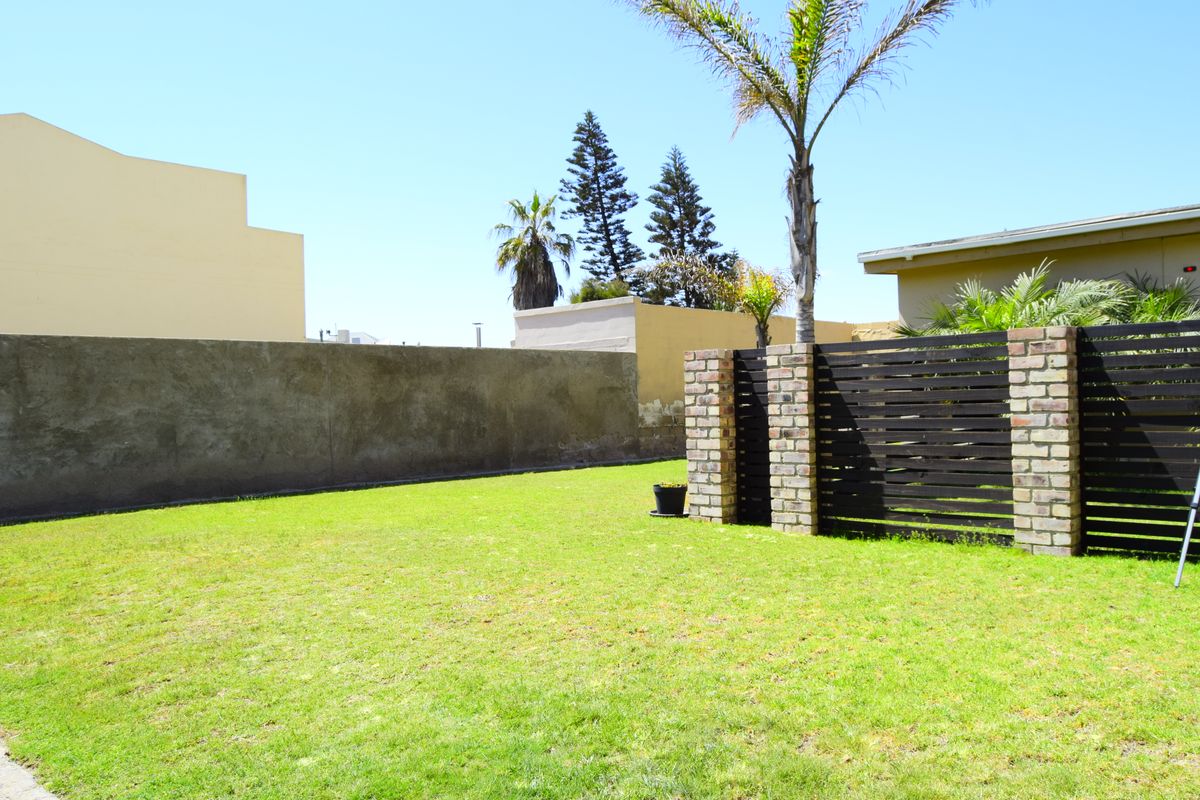 A private garden area featuring a lawn, brick boundary walls, and timber slat fencing with brick pillars.