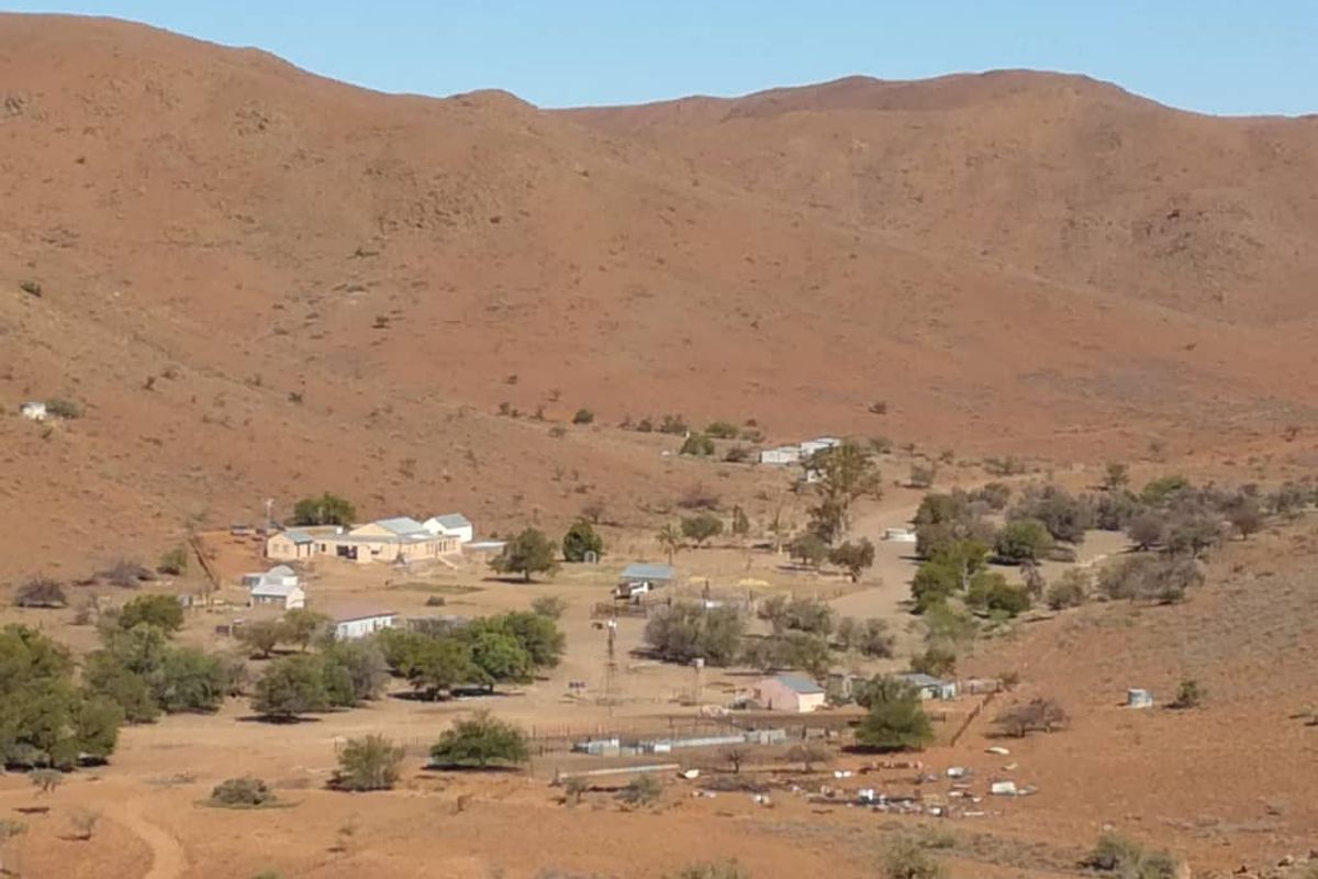 An elevated view of a rural farmstead nestled in a vast, arid landscape with surrounding mountain ranges.