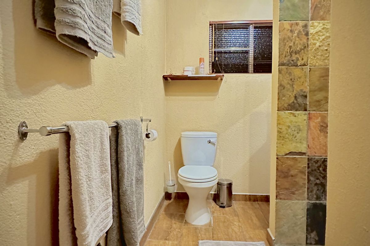 A functional bathroom featuring a toilet, a walk-in shower with multi-colored stone-look wall tiles, and wood-look floor tiling.