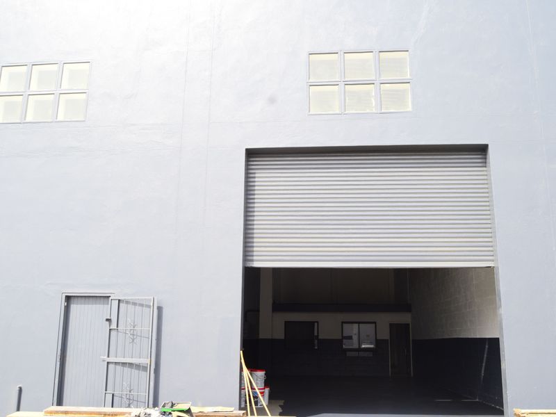 Industrial property exterior featuring a large roller shutter door, secure pedestrian entrance, and high-level windows on a freshly painted facade.
