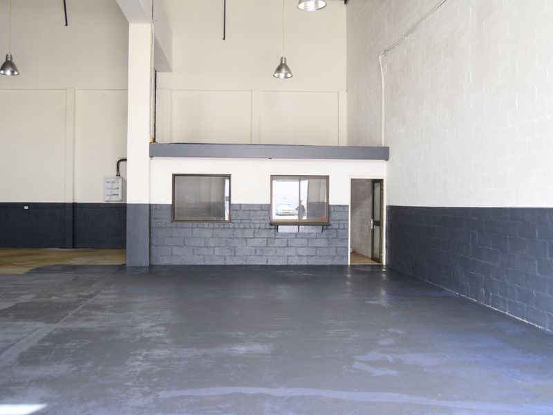Spacious industrial utility area featuring high ceilings, painted concrete flooring, and an integrated mezzanine office structure with internal windows.
