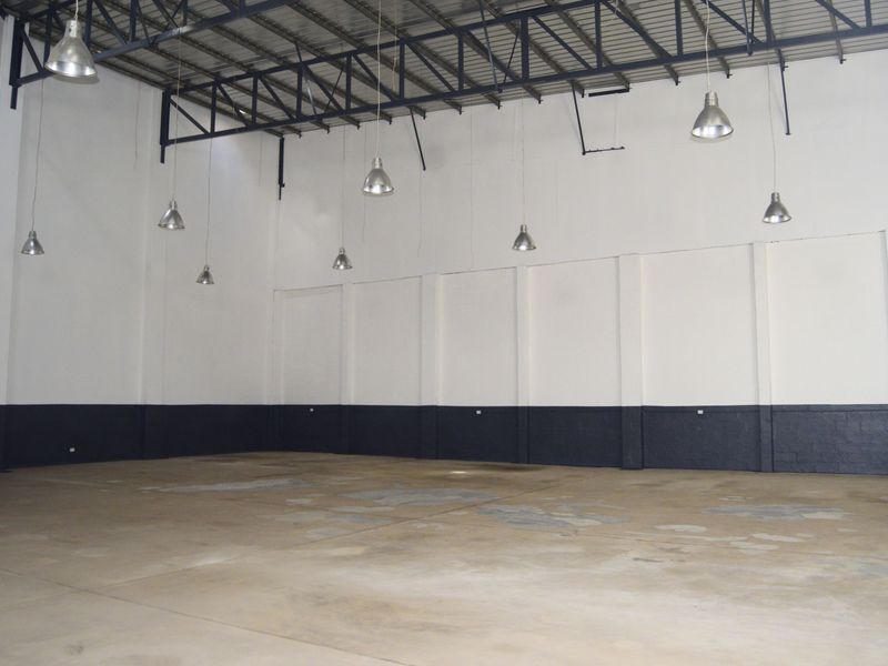 Spacious industrial warehouse unit featuring high exposed steel roof trusses, durable concrete flooring, and functional pendant lighting throughout the open floor plan.