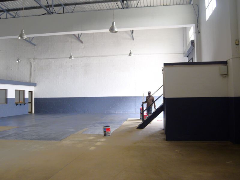 Spacious industrial warehouse unit featuring high ceilings with exposed steel trusses, concrete flooring, and a built-in service counter area.