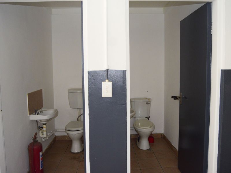 Functional industrial-style dual restroom facility featuring two separate toilet cubicles with wall-mounted basins and tiled flooring.
